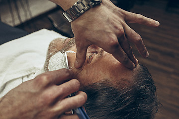 Image showing Close-up side top view handsome senior bearded caucasian man getting beard grooming in modern barbershop.