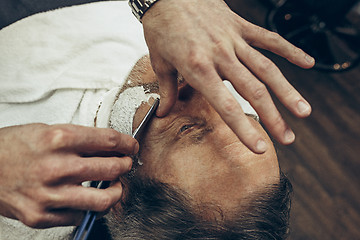 Image showing Close-up side top view handsome senior bearded caucasian man getting beard grooming in modern barbershop.