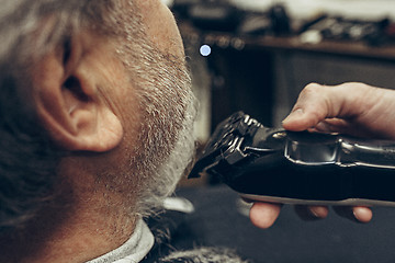 Image showing Close-up side back view handsome senior bearded caucasian man getting beard grooming in modern barbershop.