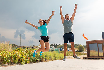 Image showing happy couple in sports clothes jumping on beach