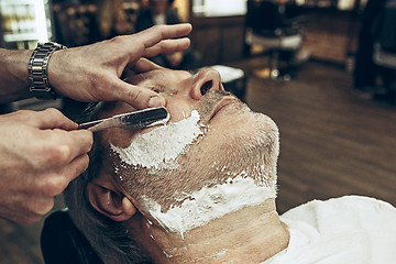 Image showing Close-up side top view handsome senior bearded caucasian man getting beard grooming in modern barbershop.