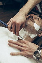 Image showing Close-up side top view handsome senior bearded caucasian man getting beard grooming in modern barbershop.