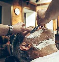 Image showing Close-up side top view handsome senior bearded caucasian man getting beard grooming in modern barbershop.