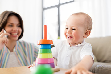 Image showing baby playing toy and mother calling on smartphone