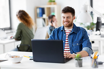 Image showing smiling creative man with laptop working at office