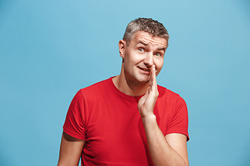 Image showing The young man whispering a secret behind her hand over blue background