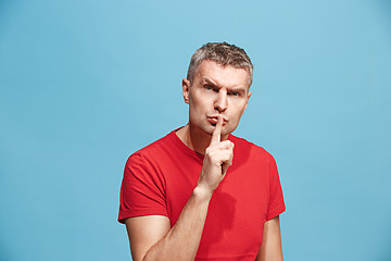 Image showing The young man whispering a secret behind her hand over blue background