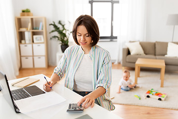 Image showing working mother counting on calculator and baby