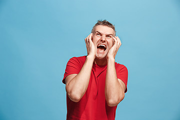 Image showing The young emotional angry man screaming on blue studio background