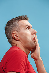 Image showing Suspiciont. Doubtful pensive man with thoughtful expression making choice against blue background
