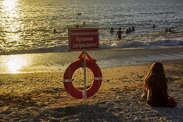 Image showing People swim in sunset sea right at the prohibitory sign