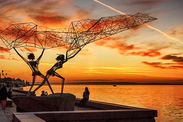 Image showing Silhouettes sculpture of fishers on lake embankment at sunset