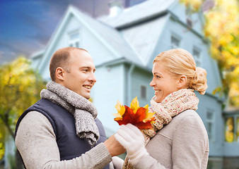 Image showing smiling couple with autumn maple leaves over house