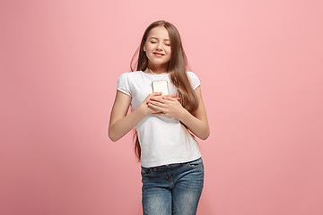 Image showing The happy teen girl with phone standing and smiling against pink background.