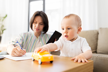 Image showing baby playing with car and mother working at home