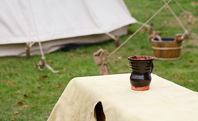 Image showing Glazed clay cup on a bench in a Medieval camp