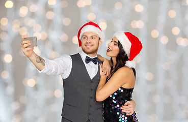 Image showing couple in santa hats taking selfie at christmas