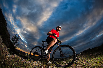 Image showing cyclist standing with mountain bike on trail at sunset