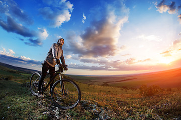 Image showing cyclist standing with mountain bike on trail at sunset