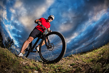 Image showing cyclist standing with mountain bike on trail at sunset