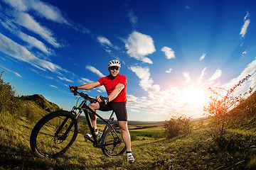 Image showing cyclist standing with mountain bike on trail at sunset