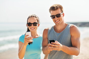 Image showing couple in sports clothes with smartphones on beach