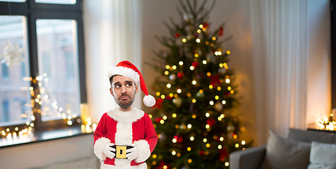 Image showing unhappy man in santa clothes over christmas tree