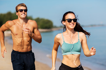 Image showing couple with earphones running along on beach