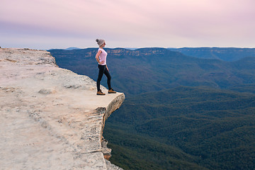 Image showing Adventurous female standing on the mountain ledge looking out to the valley beyond