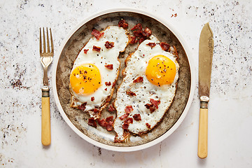 Image showing Two fresh fried eggs with crunchy crisp bacon served on rustic plate