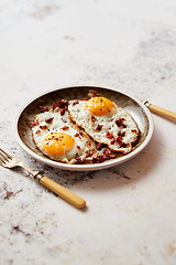 Image showing Two fresh fried eggs with crunchy crisp bacon served on rustic p