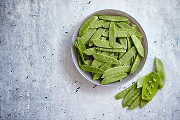 Image showing Fresh green peas in white ceramic bowl on gray stone background