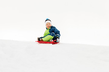 Image showing happy boy sliding on sled down snow hill in winter