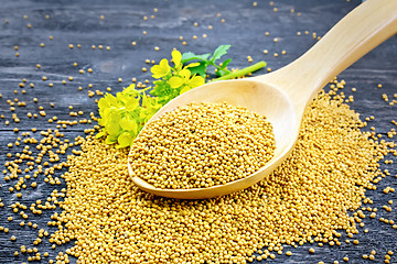 Image showing Mustard seeds in wooden spoon with flower on black board