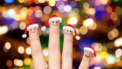 Image showing close up of four fingers in santa hats over lights