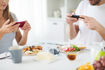 Image showing close up of couple with smartphones at breakfast