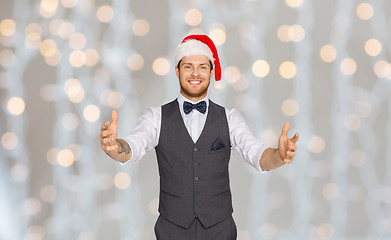 Image showing happy man in santa hat holding something imaginary