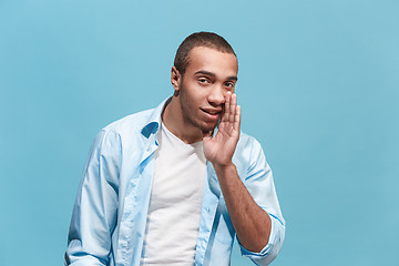 Image showing The young man whispering a secret behind her hand over blue background