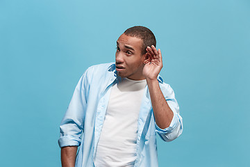 Image showing The young man whispering a secret behind her hand over blue background