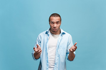 Image showing Beautiful male half-length portrait isolated on blue studio backgroud. The young emotional surprised man