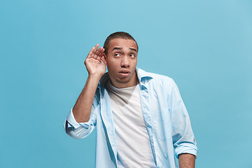 Image showing The young man whispering a secret behind her hand over blue background