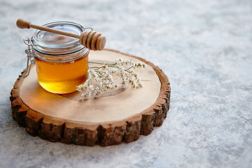 Image showing Glass jar full of fresh honey placed on slice of wood