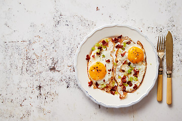 Image showing Two fresh fried eggs with crunchy crisp bacon and chive served on rustic plate