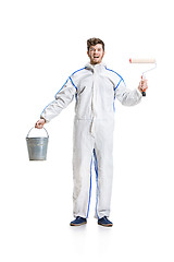 Image showing Young male decorator painting with a paint roller climbed a ladder isolated on white background.