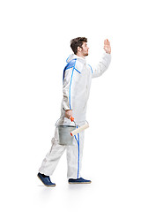 Image showing Young male decorator painting with a paint roller climbed a ladder isolated on white background.