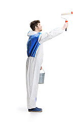 Image showing Young male decorator painting with a paint roller climbed a ladder isolated on white background.