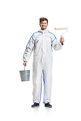 Image showing Young male decorator painting with a paint roller climbed a ladder isolated on white background.