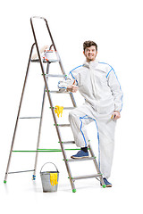 Image showing Young male decorator painting with a paint roller climbed a ladder isolated on white background.