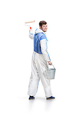 Image showing Young male decorator painting with a paint roller climbed a ladder isolated on white background.