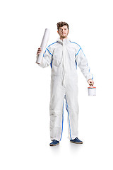 Image showing Young male decorator painting with a paint roller climbed a ladder isolated on white background.